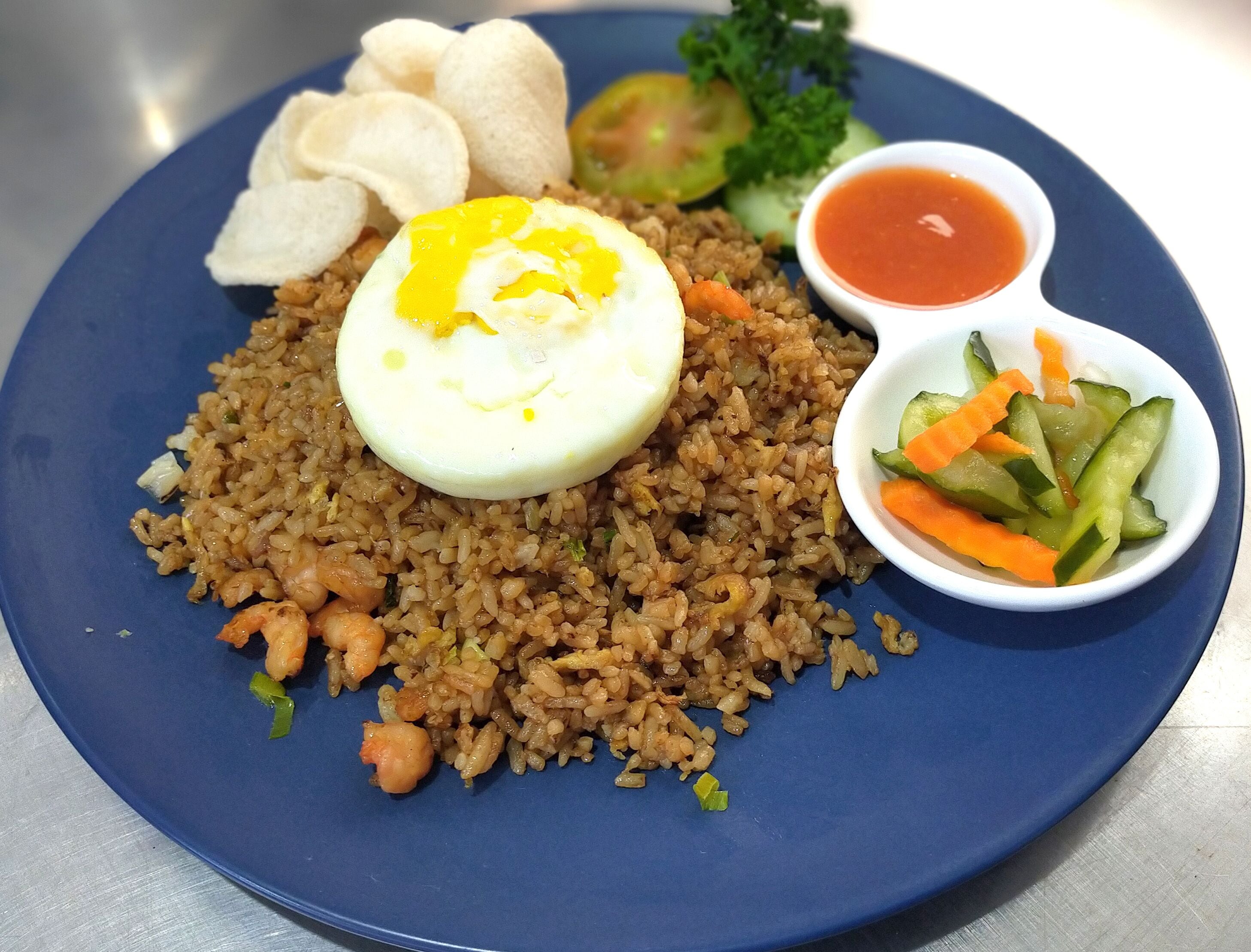A plate of fried rice with shrimp, a half-boiled egg, and a side of vegetables and sauce.
