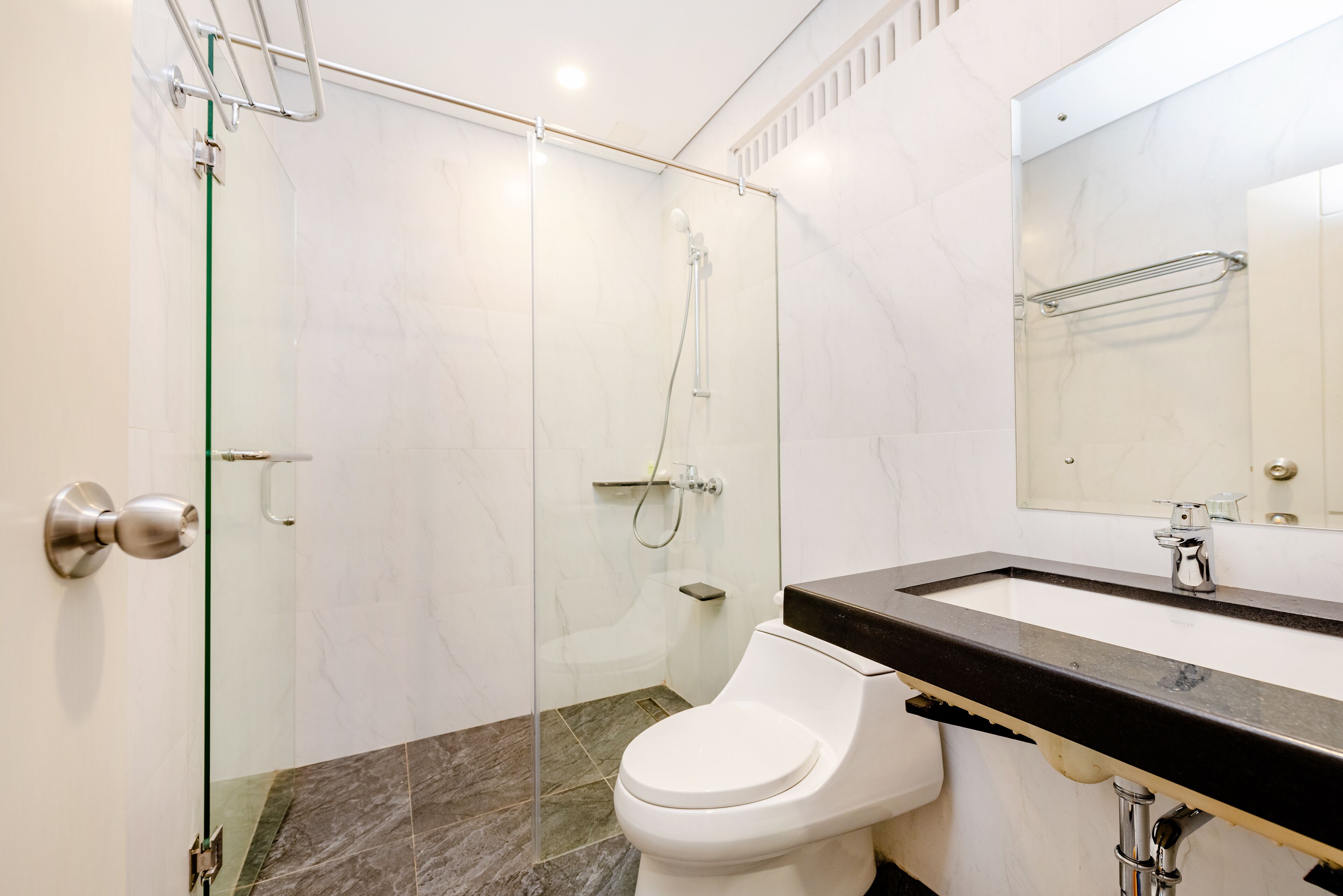 A modern bathroom with a glass-enclosed shower, a white toilet, and a black countertop sink.