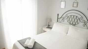 Un lit bien fait, avec du linge de lit blanc et deux serviettes enroulées, une table de chevet avec une lampe, et un mur orné de tableaux encadrés.