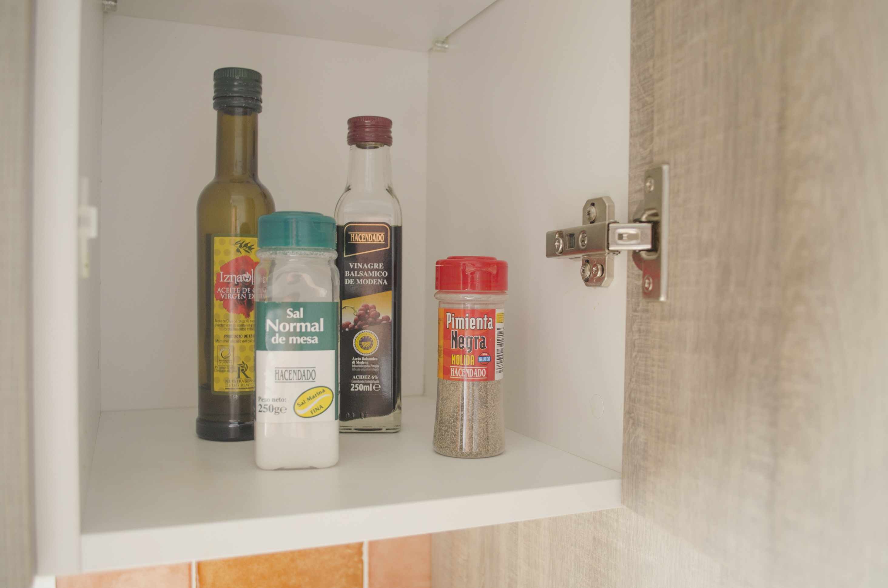 A kitchen cabinet with bottles of olive oil, balsamic vinegar, and black pepper.
