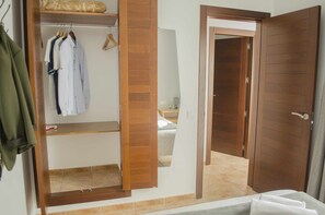 Habitación de hotel con armario de madera, cama con edredón blanco y baño a la vista, tras una puerta abierta.
