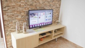 Litteänäyttöinen televisio on sijoitettu puiseen TV-telineeseen, ja taustalla on kiviseinä.