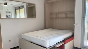 A compact room with a bed, a built-in wardrobe, a mirror, and a ceiling fan. - Equipped studio with parking in Balaruc-les-Bains (Balaruc-les-Bains)
