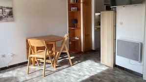 A compact living space with a dining table and chairs, a built-in bookshelf, a TV, and a kitchenette area. - Equipped studio with parking in Balaruc-les-Bains (Balaruc-les-Bains)