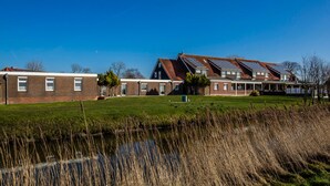 A row of modern houses with solar panels, a grassy field, and a body of water. - Logia Hotel garni (Neuharlingersiel)