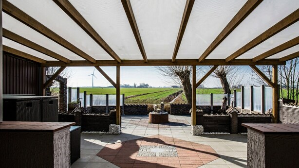 A covered outdoor patio with a view of wind turbines and fields. - Logia Hotel garni (Neuharlingersiel)