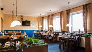 A restaurant with multiple tables and chairs, pendant lighting, and large windows with curtains. - Logia Hotel garni (Neuharlingersiel)