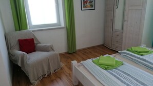 A room with a wooden floor, a chair with a red pillow, a bed with striped bedding, and a green curtain. - Ferienwohnung Gundacker (Dobersberg)