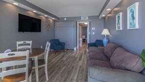 A modern living room with a flat-screen TV, a dining table with chairs, a sofa, and a hallway leading to another room. - Atlantica 803 (Myrtle Beach)