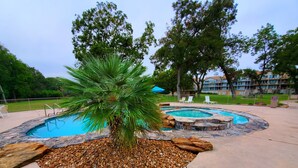 Una piscina con una palmera y zona de hidromasaje, rodeada de guijarros y rocas.