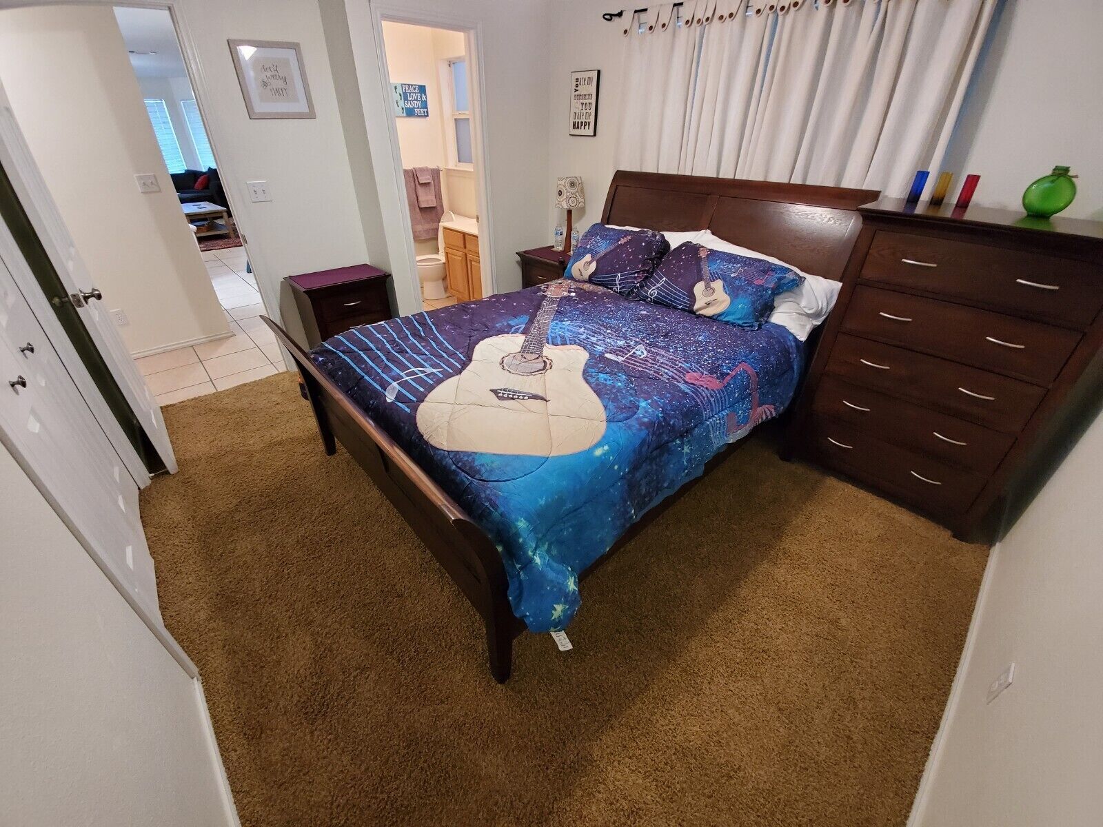 Une chambre à coucher avec un lit dont la tête de lit est décorée d’un motif de guitare, une commode et une table de chevet.