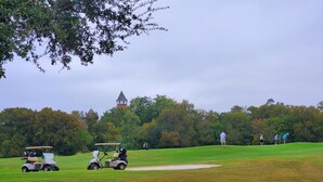 Un campo de golf con un búnker, un carrito de golf y un edificio a lo lejos.