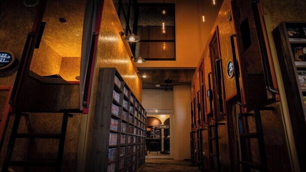 A narrow hallway with bookshelves on both sides, a staircase, and a small reading area with a table and chairs. - eeGee STAY Kamata (Tokyo)