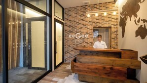 A reception area with a brick wall, a wooden reception desk, and a glass door leading to a room. - eeGee STAY Kamata (Tokyo)
