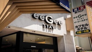 The exterior of a hotel named 'eeGee Stay' with a modern design, featuring a large glass entrance and signage indicating it is a capsule hotel with 4-6 rooms. - eeGee STAY Kamata (Tokyo)