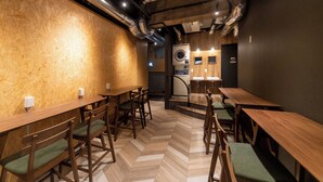 A restaurant with wooden tables and chairs, a herringbone floor, and a visible restroom area with sinks and a toilet. - eeGee STAY Kamata (Tokyo)