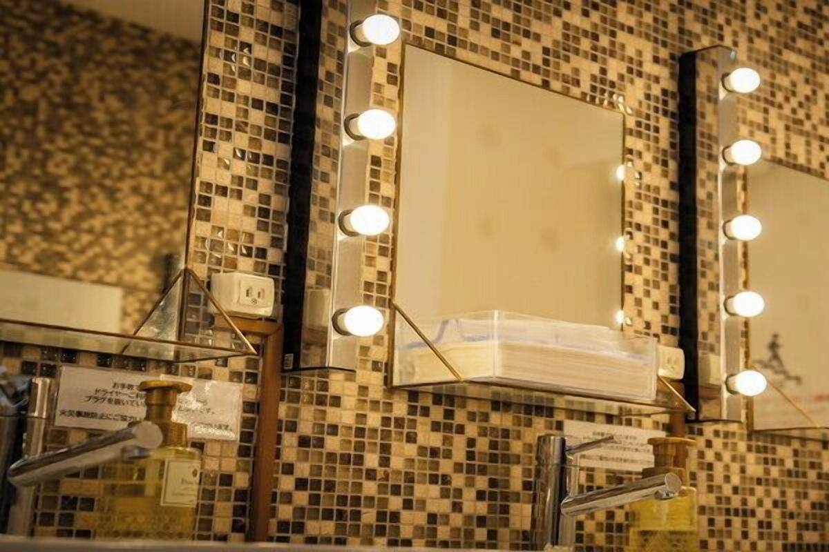 Une salle de bain avec trois miroirs, chacun étant entouré de lumières, et un mur recouvert de carreaux.