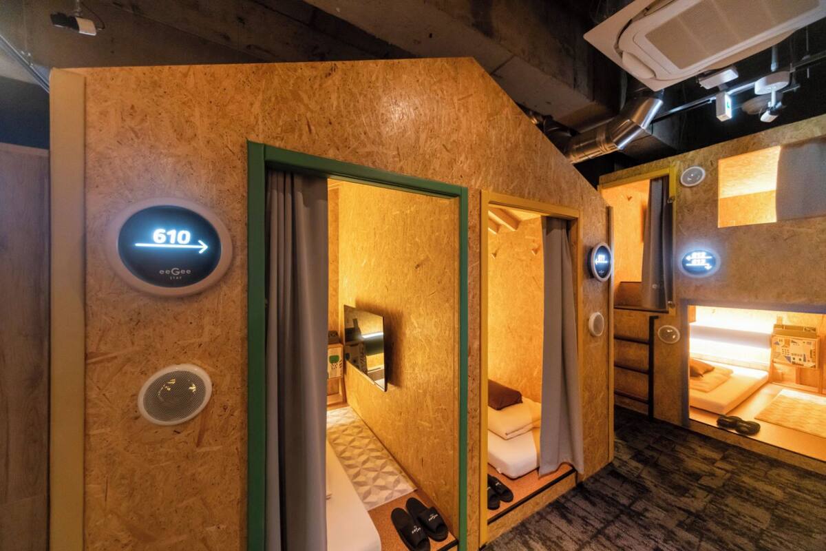Une chambre d’hôtel moderne avec un intérieur en bois, un lit, un petit coin salon et un écran numérique affichant le numéro de chambre : 610.