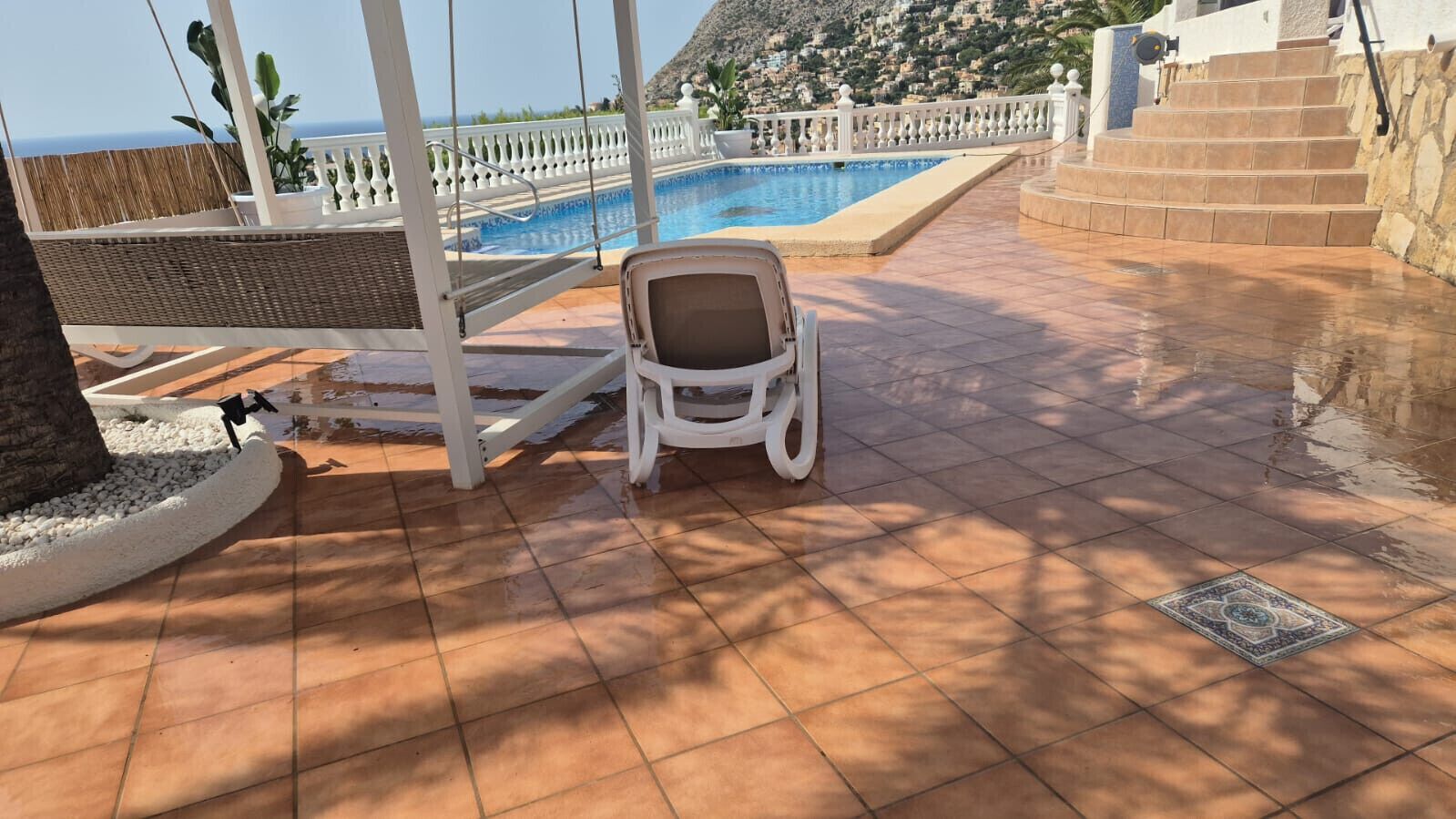 Uma área à beira da piscina com uma cadeira, um corrimão branco e vista para o mar.