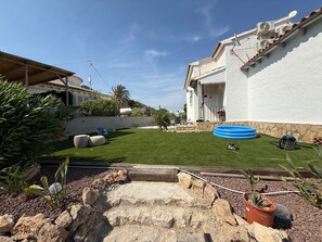 Un patio trasero bien cuidado con césped, una piscina inflable azul y un muro de piedra.
