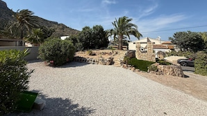 Zona residencial amb carrer de grava, palmeres i una casa amb mur de pedra i antena parabòlica.