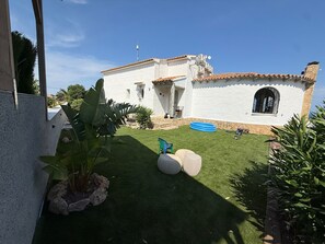 A white building with a tiled roof, a small lawn, and a blue inflatable pool. - Casa Sueño para 6 Personas (Calpe)