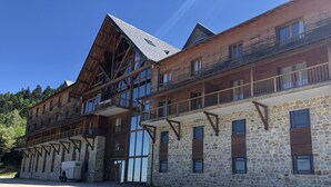 A multi-story building with stone walls and wooden balconies, featuring large windows and a sloped roof. - 4-person apartment, at the foot of the slopes, Ariège (Ustou)