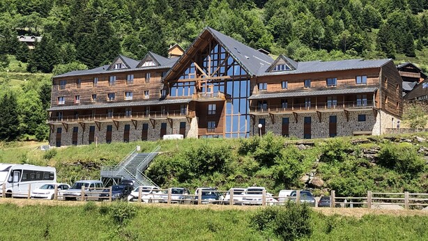 A large wooden lodge with multiple balconies and a stone facade, surrounded by lush greenery and a parking area. - 4-person apartment, at the foot of the slopes, Ariège (Ustou)
