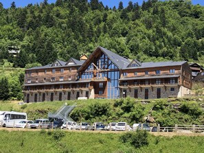 A large wooden lodge with multiple balconies and a stone facade, surrounded by lush greenery and a parking area. - 4-person apartment, at the foot of the slopes, Ariège (Ustou)