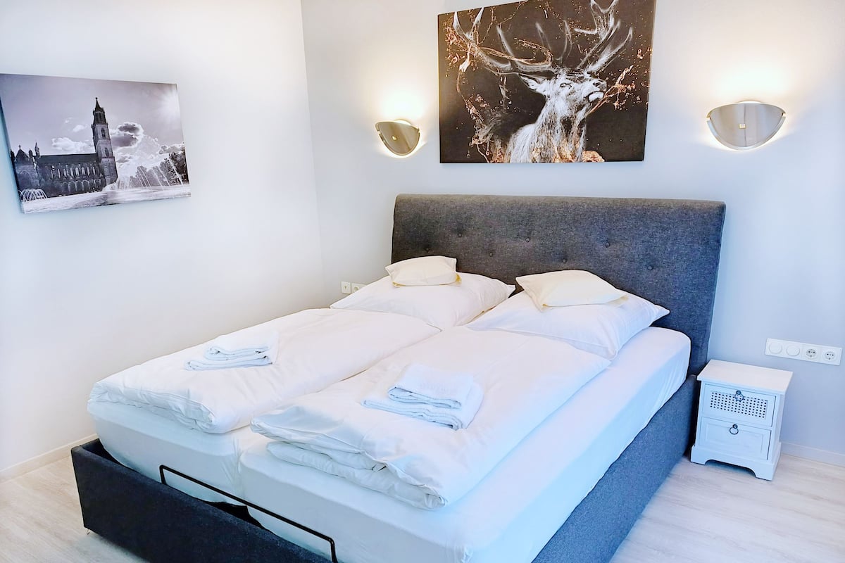 A modern hotel room with a large bed, two bedside tables, a wall-mounted light fixture, and a framed picture of a deer.