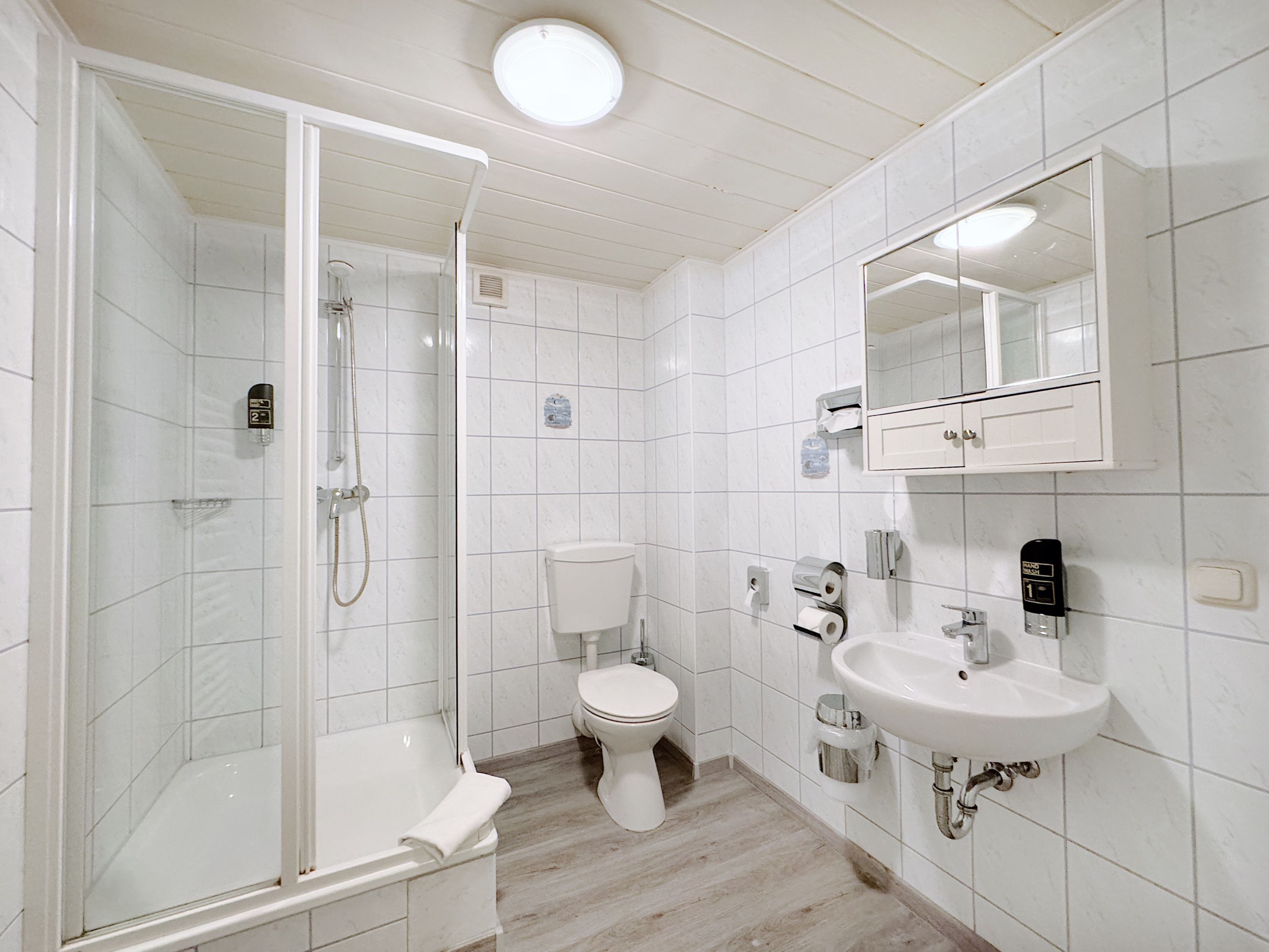 Un bany modern amb dutxa de vidre, vàter i un lavabo amb mirall a la part superior.
