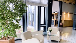 Un interior modern amb una finestra gran, una planta en test i dos butaques blanques.