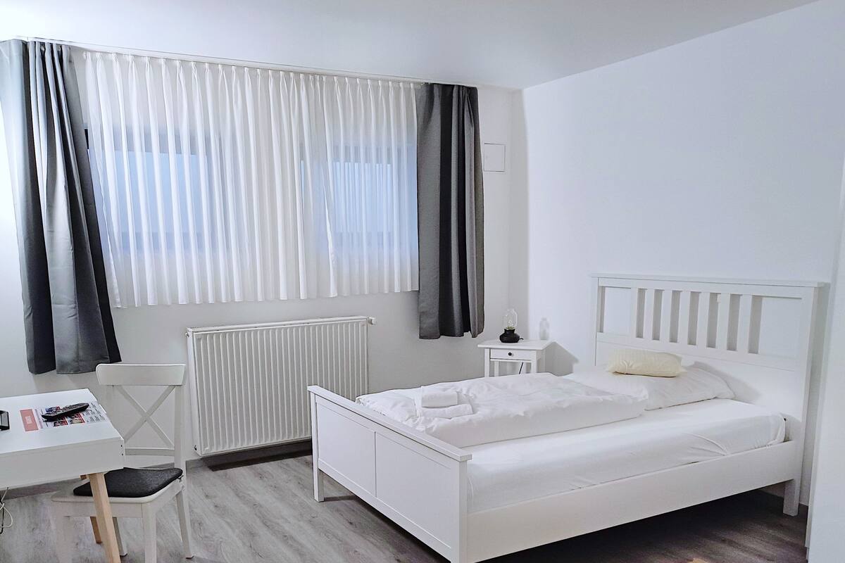 A white bedroom with a bed, a desk, and a chair.
