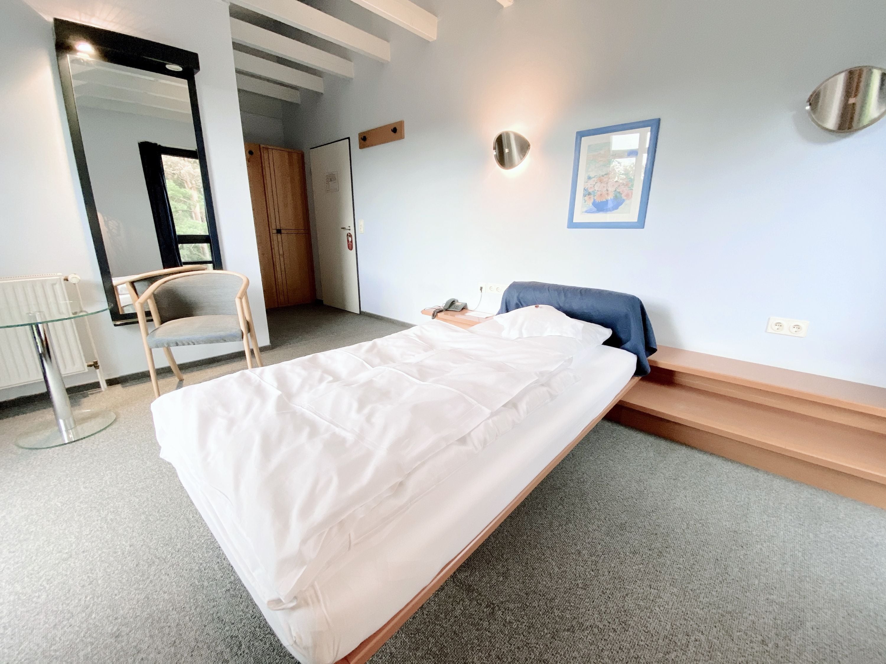 A bedroom with a bed, a chair, a desk, a mirror, and a door.
