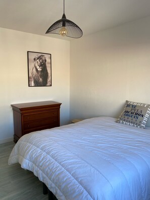 A bedroom with a bed, a wooden dresser, a wall-mounted picture of a lion, a black pendant light, and a pillow with text.