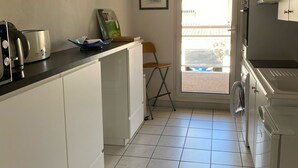 Uma cozinha compacta com armários brancos, uma torradeira de aço inoxidável, um lustre e uma porta que dá para uma varanda.
