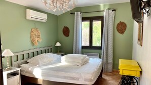 Ein Schlafzimmer mit Bett, Nachttisch, Lampe, Klimaanlage, einem fenster mit Vorhängen und einem Fernseher.