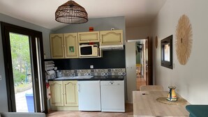 Eine kleine Küche mit Mikrowelle, Kühlschrank und Spüle. Ein Esstisch mit Stühlen und eine hängende Leuchte sind vorhanden.