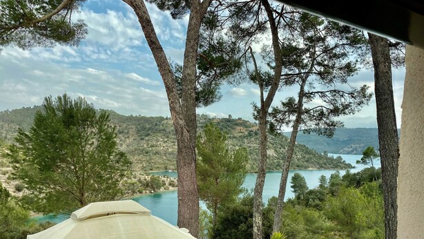 Eine Terrasse mit Terrakotta-Pflanzgefäßen, einem weißen Sonnenschirm und Blick auf einen See und Hügel.