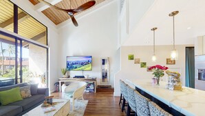 A spacious living area with a large TV, a dining area with a long counter, and a ceiling fan. - Luxury Maui Condo with Direct Beach Access (Kihei)