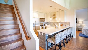 A modern kitchen with a central island, bar stools, and a staircase. - Luxury Maui Condo with Direct Beach Access (Kihei)