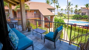 A balcony with a sofa and table, overlooking a swimming pool and lush greenery. - Luxury Maui Condo with Direct Beach Access (Kihei)