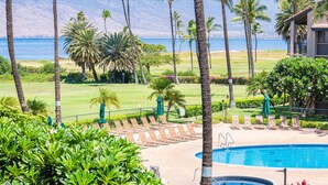 A pool area with a view of the ocean, surrounded by palm trees and a golf course. - Luxury Maui Condo with Direct Beach Access (Kihei)