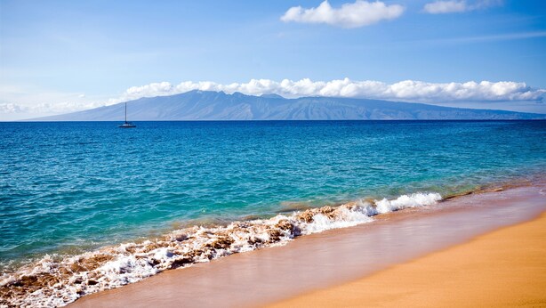 A beach with clear turquoise water, a sandy shore, and a distant mountain range. - Luxury Maui Condo with Direct Beach Access (Kihei)