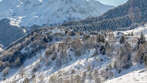 Un village de montagne enneigé, avec des bâtiments de style chalet, entouré de pentes boisées et de sommets enneigés.