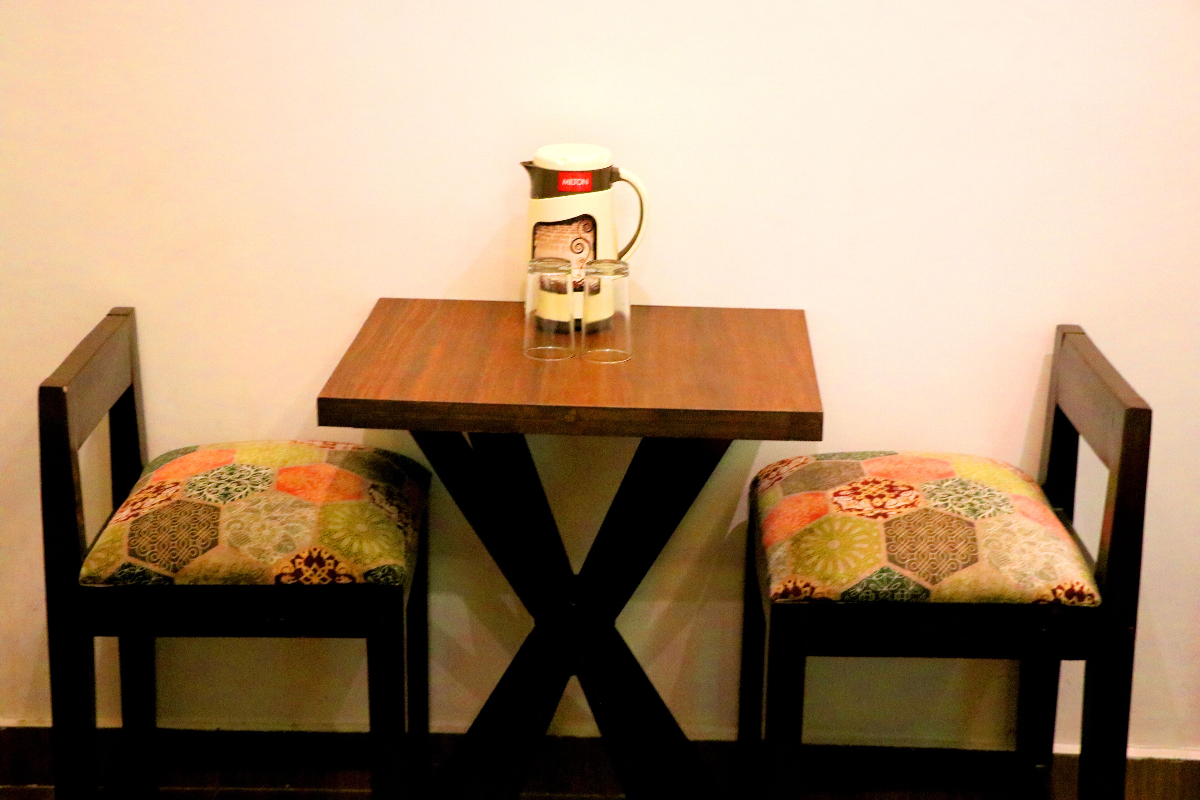 A small table with a coffee maker and two chairs with patterned cushions.