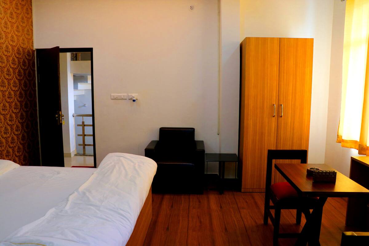 A hotel room with a bed, a desk, a chair, a wardrobe, and a lamp.