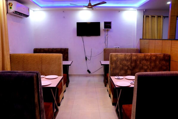 A restaurant with booths and tables, ceiling fan, TV, and air conditioning unit. - Surya Hotel (Balrampur)