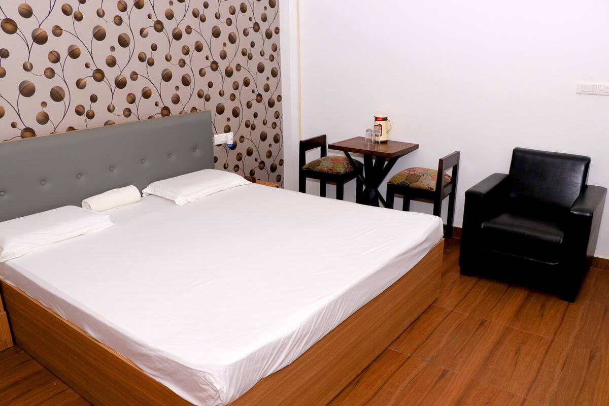A hotel room with a large bed, a small table with chairs, and a black armchair.