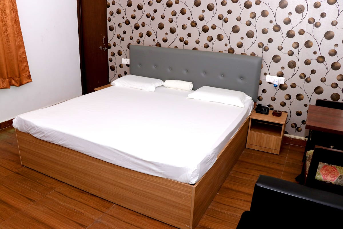 A neatly made bed with a grey headboard, wooden flooring, and a patterned wallpaper.